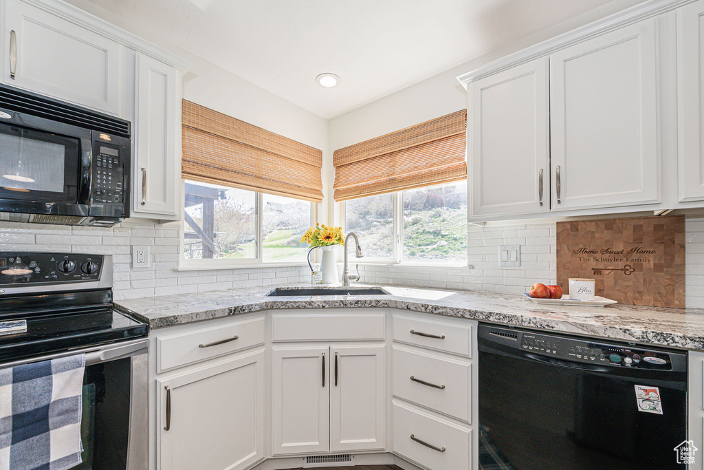Kitchen featuring black appliances, light stone counters, white cabinets, and tasteful backsplash