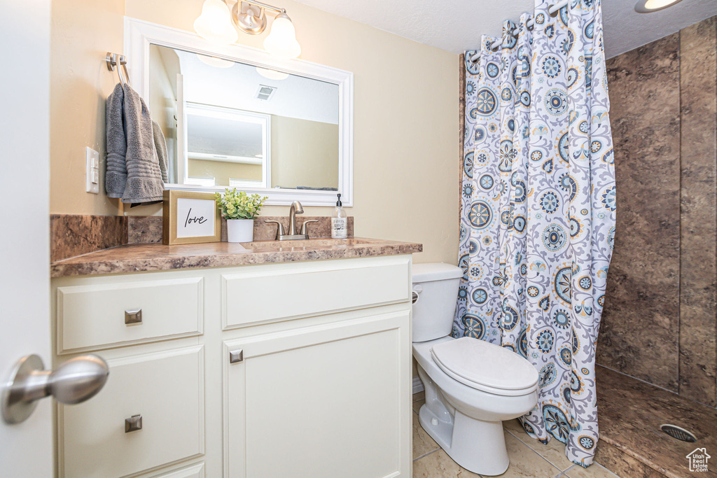 Bathroom featuring tile flooring, a textured ceiling, toilet, vanity, and curtained shower