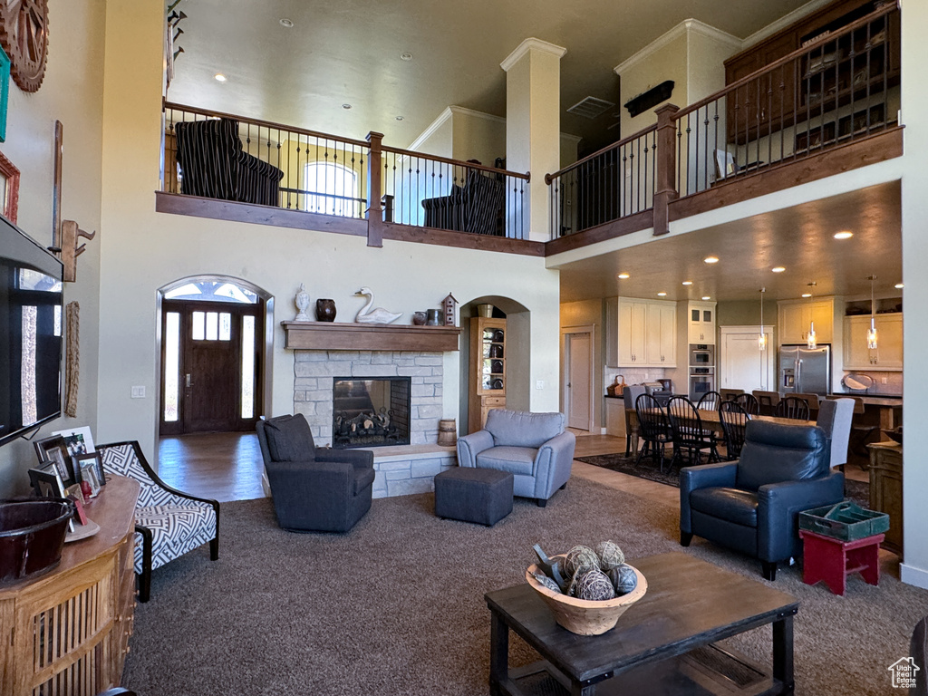 Living room featuring a high ceiling, dark carpet, a stone fireplace, and crown molding