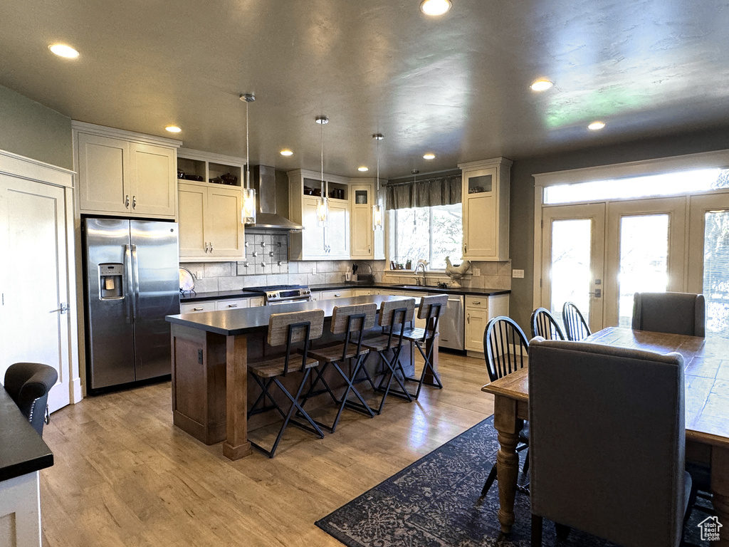 Kitchen featuring a kitchen island, french doors, light hardwood / wood-style flooring, wall chimney exhaust hood, and appliances with stainless steel finishes