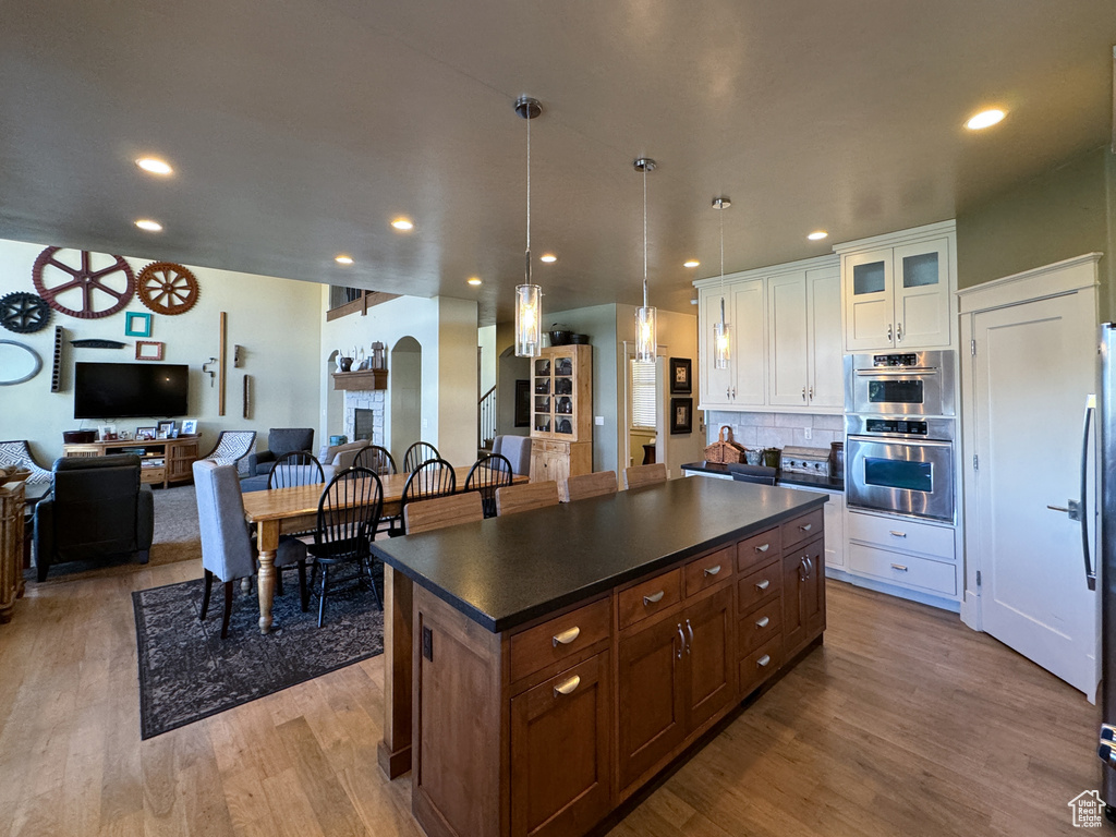 Kitchen featuring backsplash, stainless steel double oven, light hardwood / wood-style flooring, white cabinets, and a center island