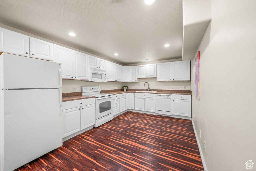 Kitchen with white cabinets, white appliances, dark wood-type flooring, and sink