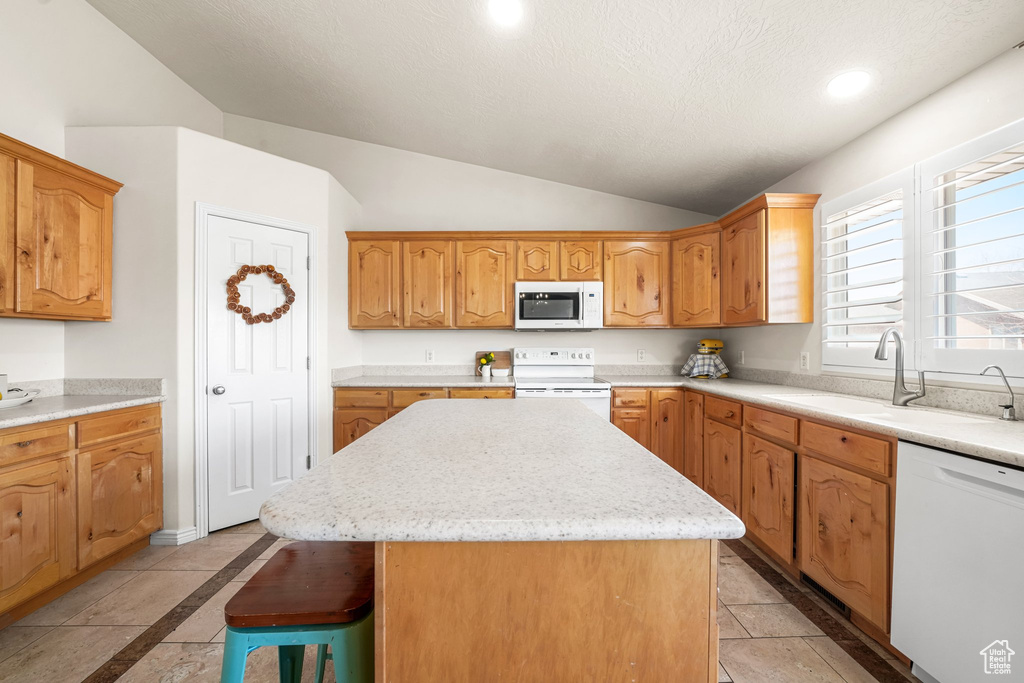 Kitchen with light tile floors, a center island, white appliances, sink, and vaulted ceiling