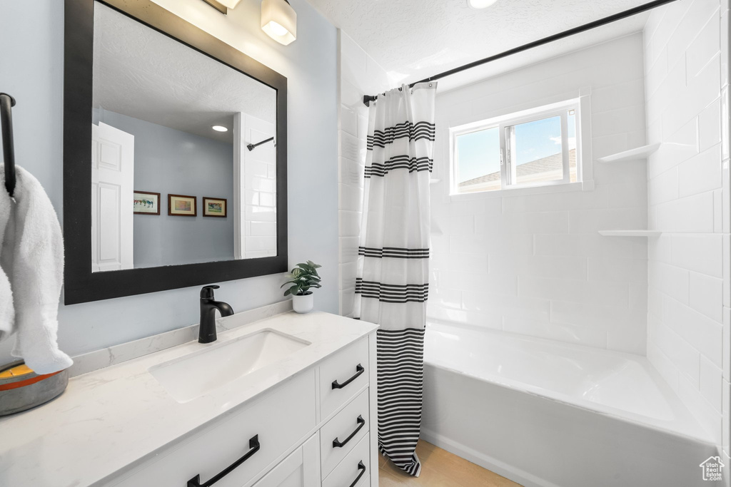 Bathroom with a textured ceiling, vanity, and shower / bathtub combination with curtain