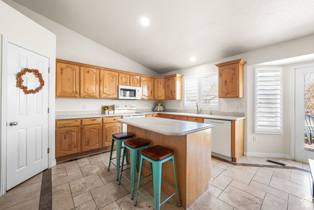 Kitchen featuring a center island, lofted ceiling, white appliances, light tile floors, and a kitchen breakfast bar