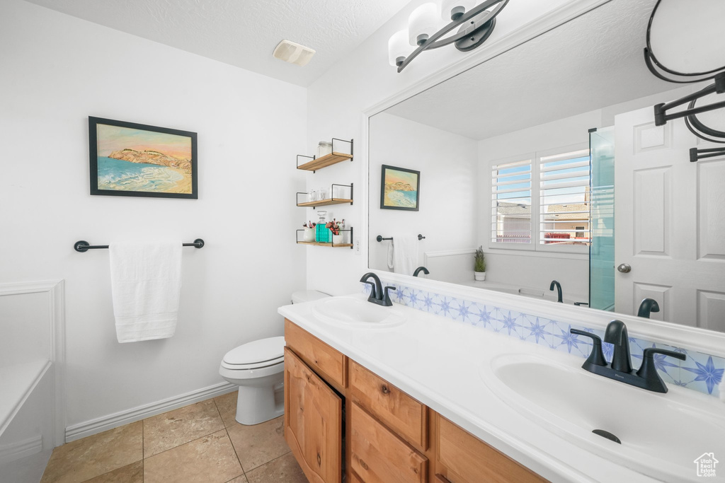 Bathroom featuring tile flooring, double sink, a textured ceiling, toilet, and vanity with extensive cabinet space