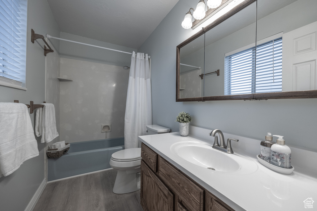 Full bathroom with toilet, oversized vanity, shower / tub combo with curtain, and hardwood / wood-style floors