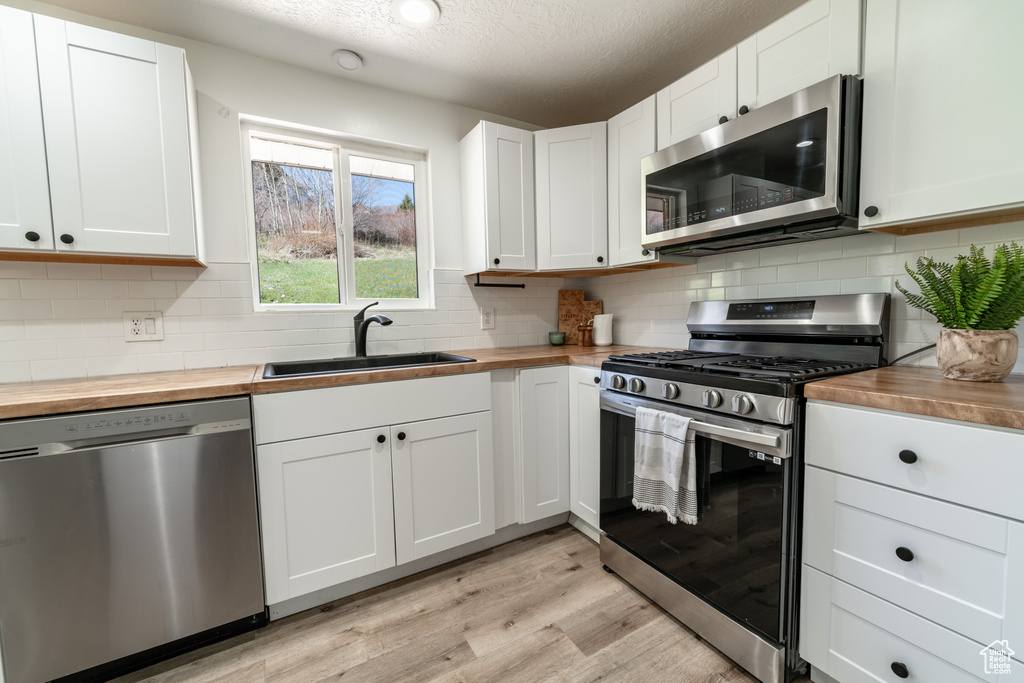 Kitchen featuring appliances with stainless steel finishes, sink, light hardwood / wood-style floors, white cabinetry, and butcher block countertops