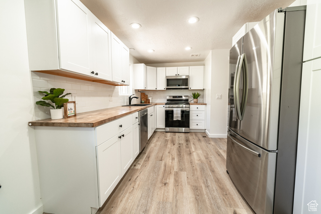 Kitchen featuring appliances with stainless steel finishes, backsplash, light hardwood / wood-style flooring, and white cabinets