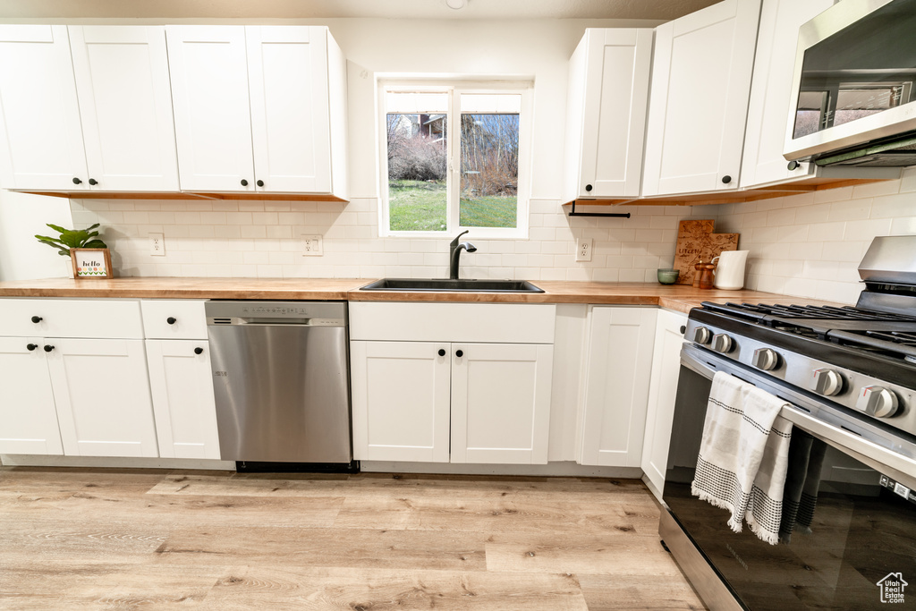 Kitchen featuring appliances with stainless steel finishes, butcher block counters, backsplash, and light hardwood / wood-style floors