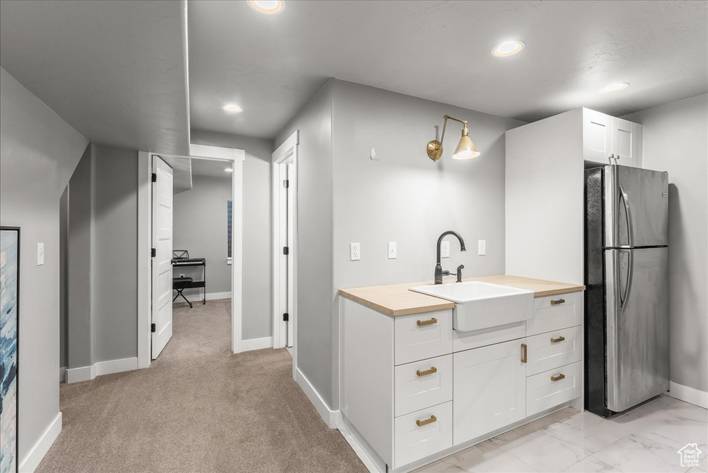 Kitchen featuring sink, stainless steel fridge, light carpet, and white cabinets