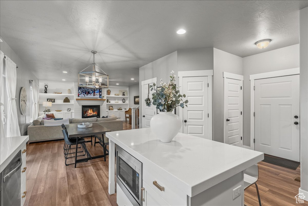 Kitchen with white cabinets, appliances with stainless steel finishes, built in shelves, light hardwood / wood-style flooring, and a kitchen bar