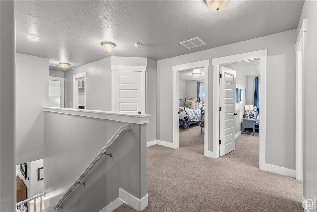 Hallway with light colored carpet and a textured ceiling