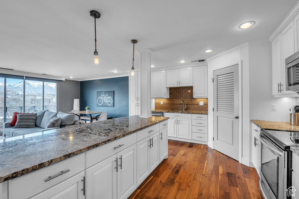 Kitchen with decorative light fixtures, white cabinets, dark stone counters, and wood-type flooring
