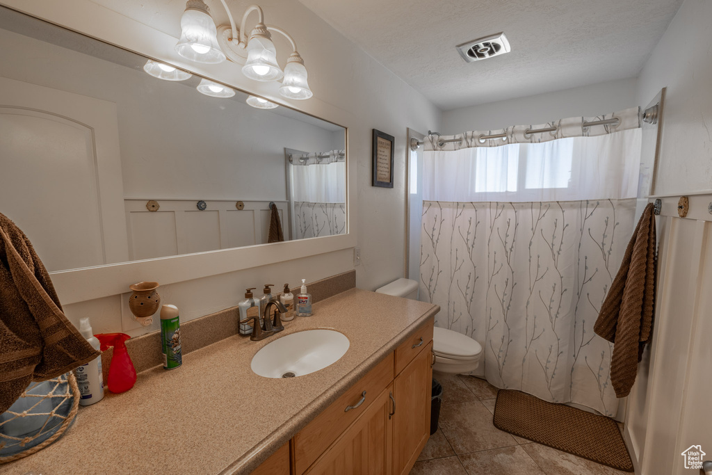 Bathroom with tile flooring, toilet, an inviting chandelier, and vanity