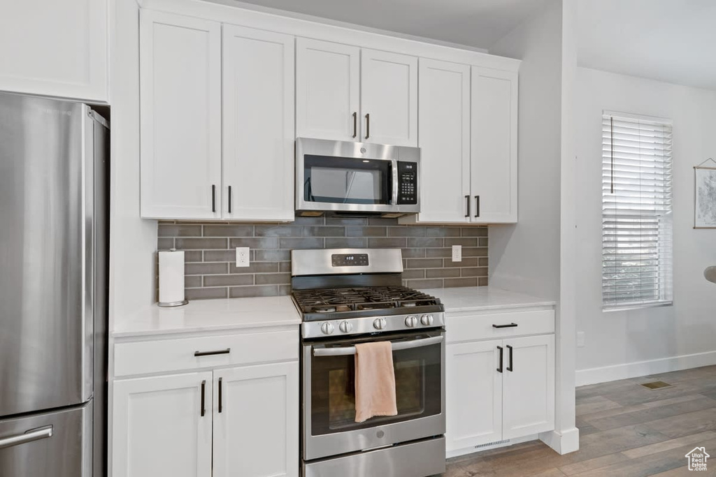 Kitchen with stainless steel appliances, light wood-type flooring, white cabinets, and backsplash
