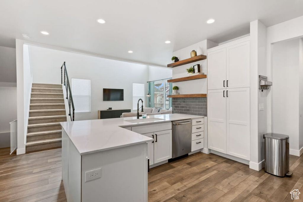 Kitchen featuring backsplash, sink, white cabinetry, stainless steel dishwasher, and light wood-type flooring