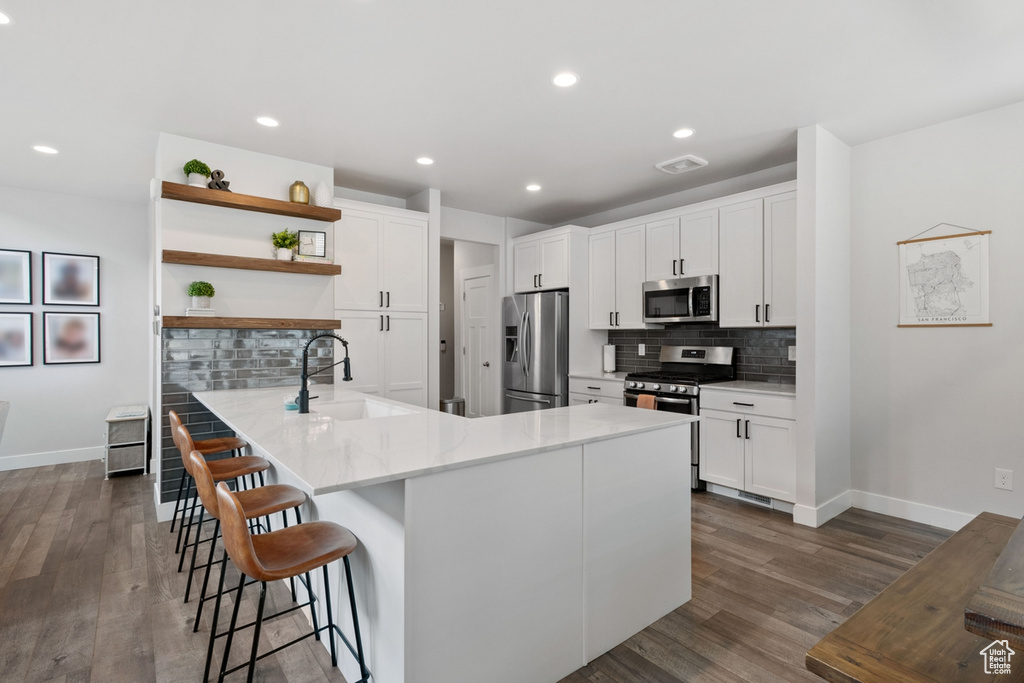 Kitchen featuring stainless steel appliances, dark wood-type flooring, backsplash, sink, and white cabinetry