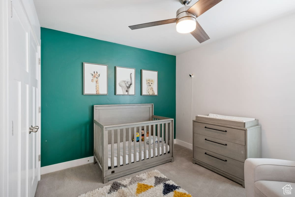 Bedroom with light colored carpet, ceiling fan, and a nursery area