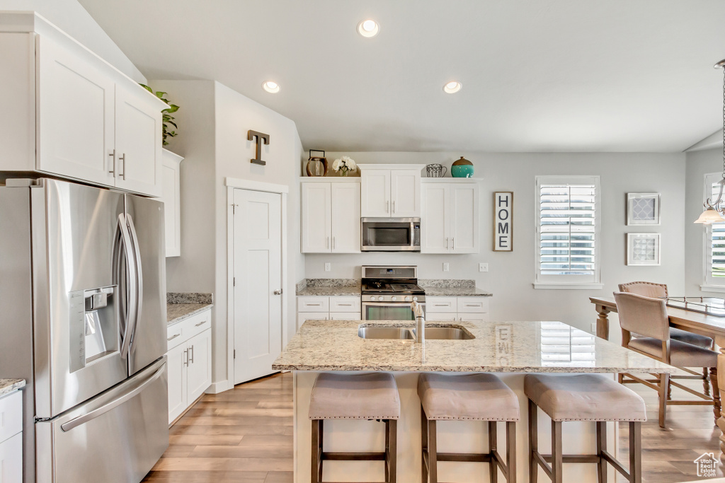 Kitchen featuring white cabinets, a center island with sink, stainless steel appliances, and light hardwood / wood-style flooring