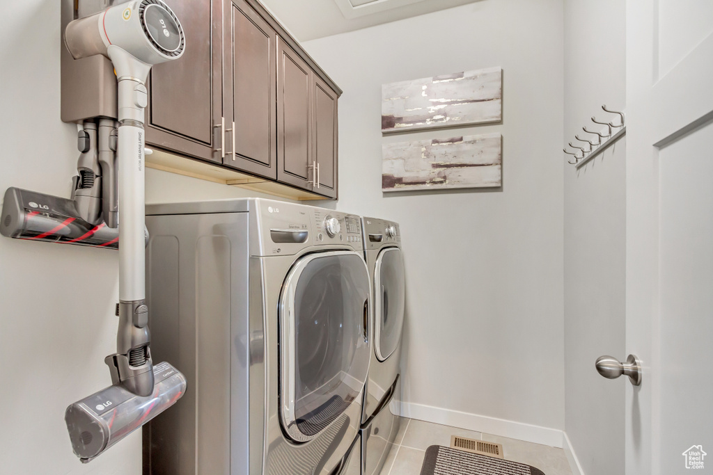 Clothes washing area with cabinets, washer and dryer, and light tile floors