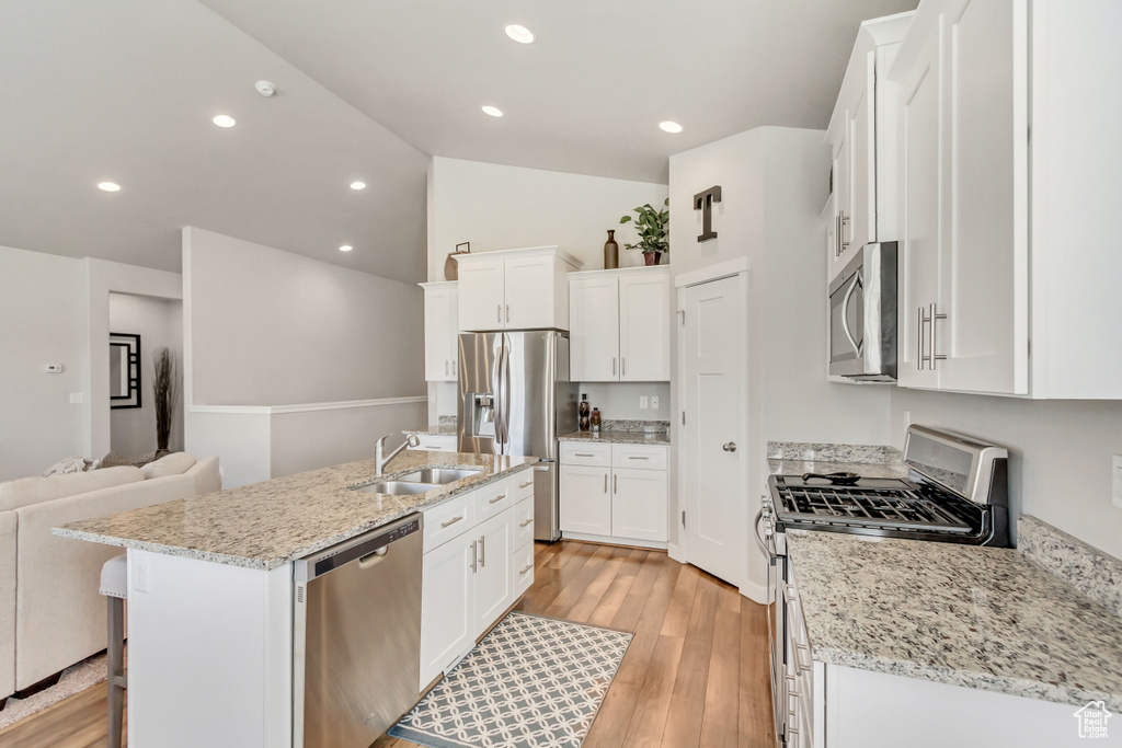 Kitchen featuring appliances with stainless steel finishes, light stone counters, light hardwood / wood-style floors, white cabinets, and a kitchen island with sink