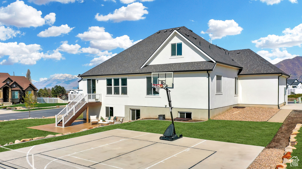 Rear view of property featuring basketball hoop, a mountain view, and a yard