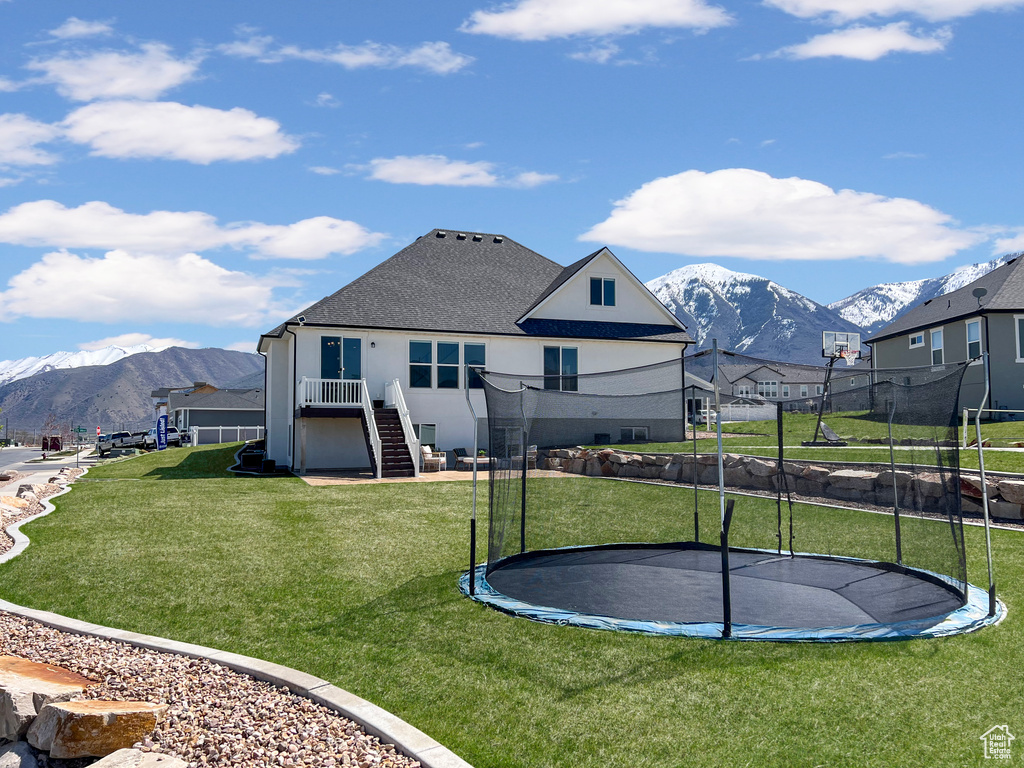 Rear view of property featuring a mountain view, a trampoline, and a lawn
