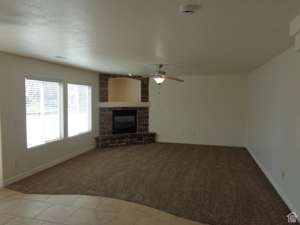 Unfurnished living room with a fireplace, brick wall, light carpet, and ceiling fan