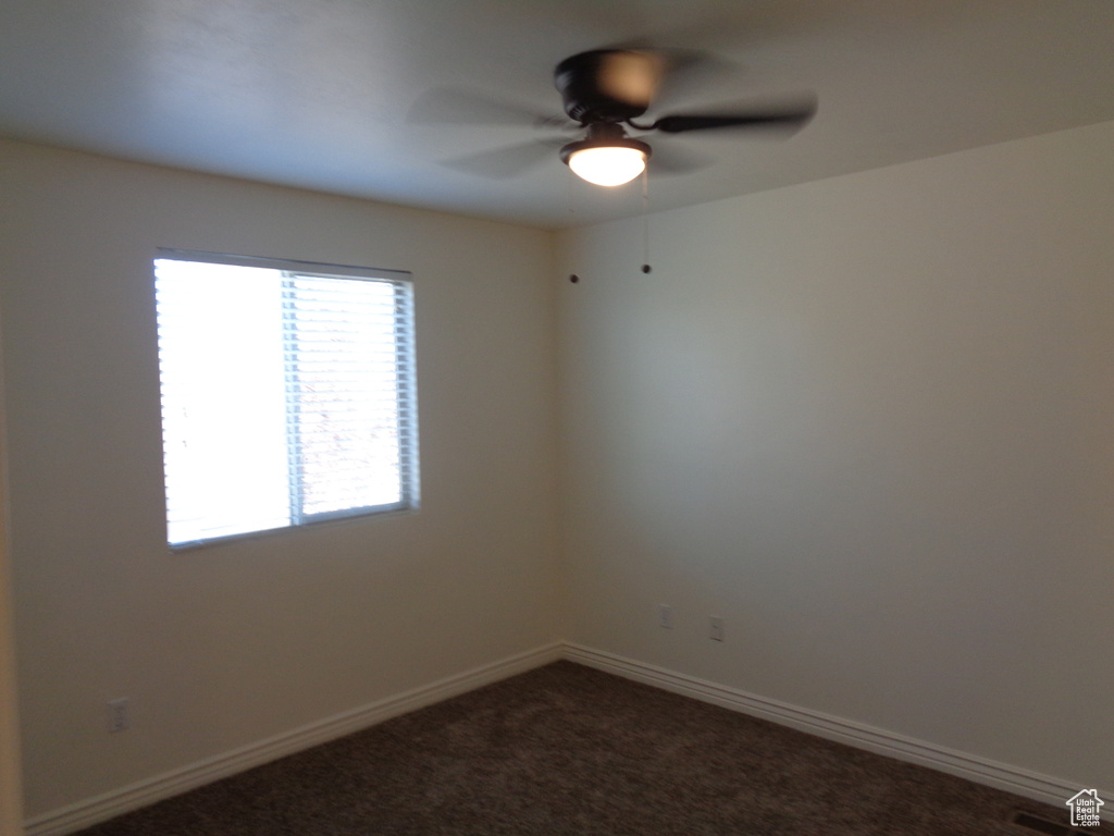 Unfurnished room featuring ceiling fan and dark colored carpet
