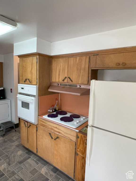 Kitchen with dark tile flooring, white appliances, and washer / dryer
