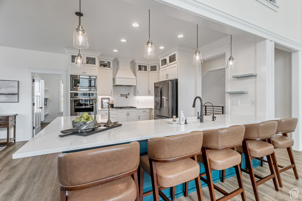 Kitchen featuring white cabinets, stainless steel appliances, light wood-type flooring, backsplash, and premium range hood