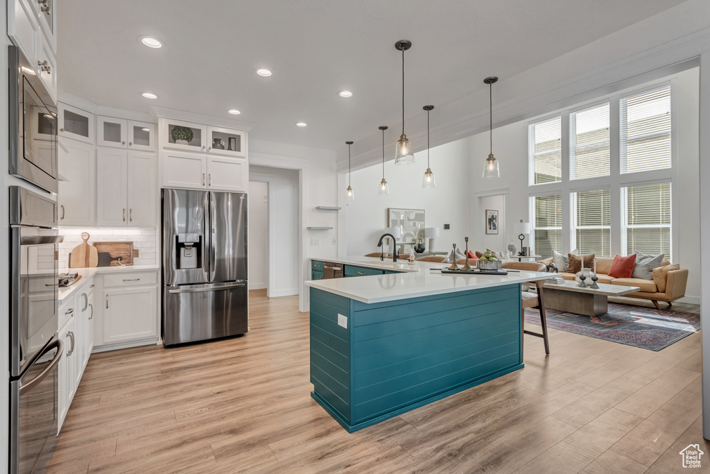 Kitchen with hanging light fixtures, light wood-type flooring, white cabinetry, and stainless steel fridge with ice dispenser