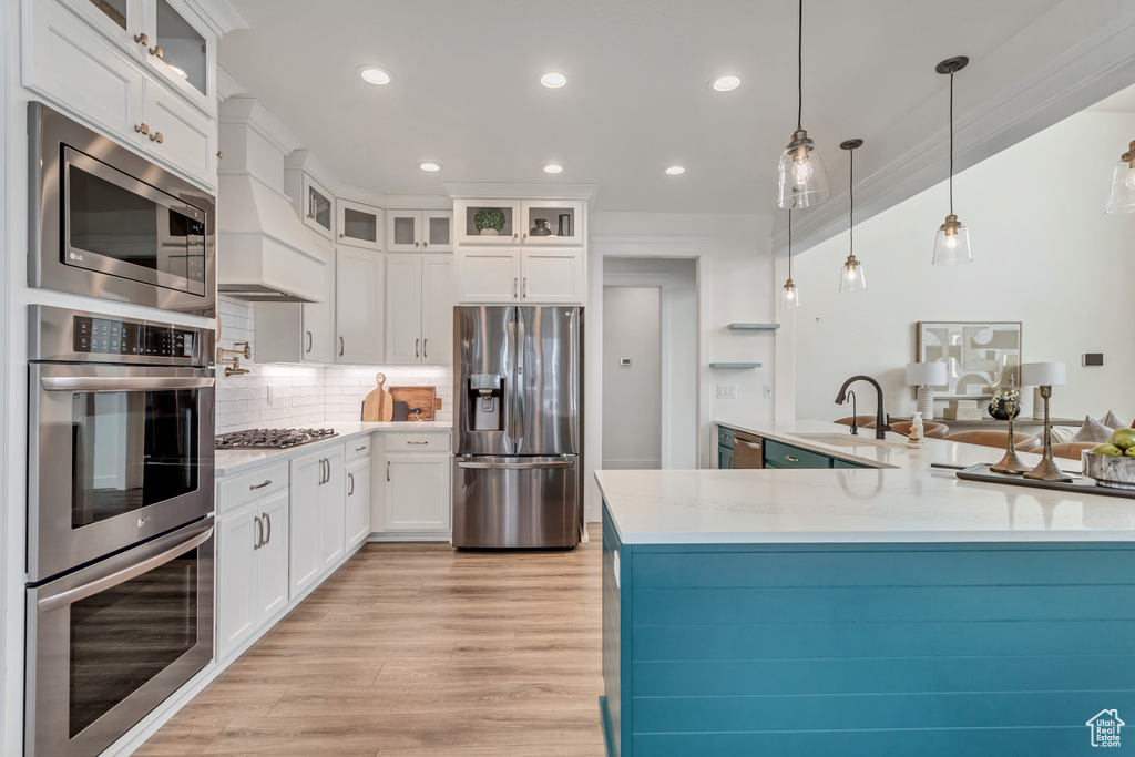 Kitchen featuring white cabinets, backsplash, appliances with stainless steel finishes, pendant lighting, and light hardwood / wood-style flooring