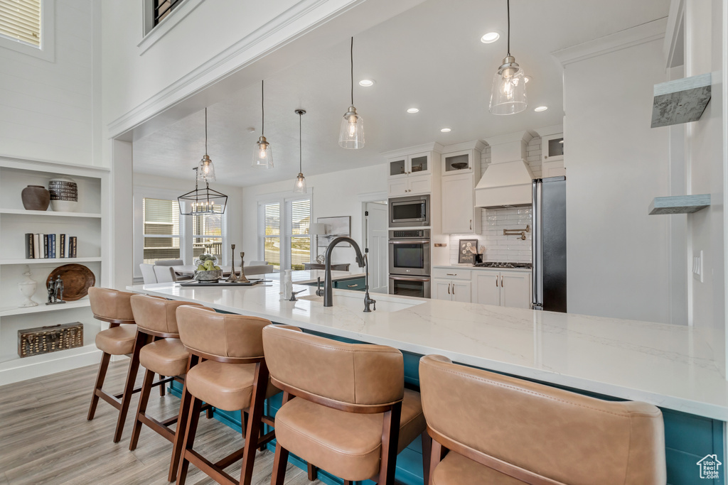 Kitchen featuring appliances with stainless steel finishes, custom exhaust hood, a notable chandelier, a kitchen breakfast bar, and white cabinetry