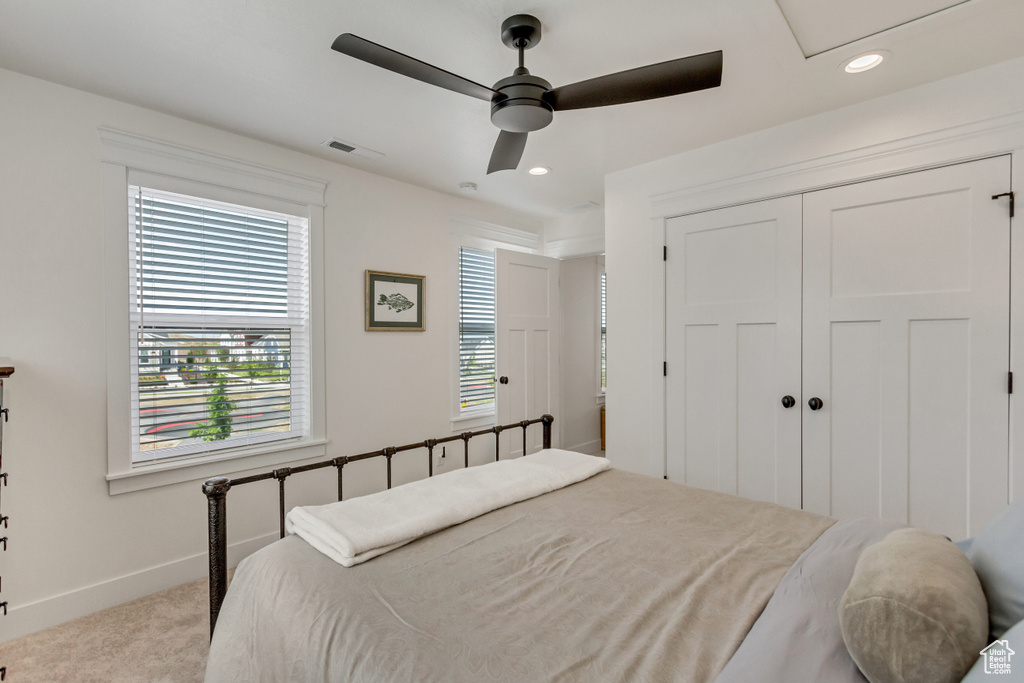 Carpeted bedroom featuring multiple windows, ceiling fan, and a closet