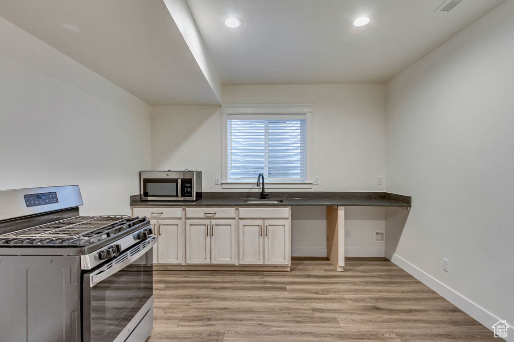Kitchen featuring appliances with stainless steel finishes, light wood-type flooring, white cabinetry, and sink