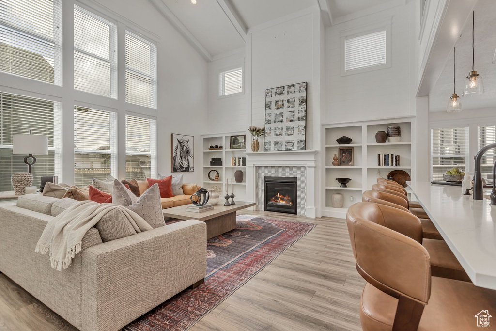 Living room with high vaulted ceiling, a wealth of natural light, built in shelves, and light wood-type flooring