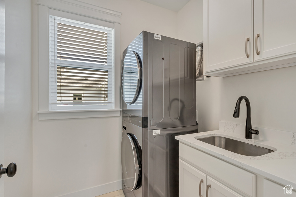 Clothes washing area with cabinets, sink, stacked washer / dryer, and plenty of natural light