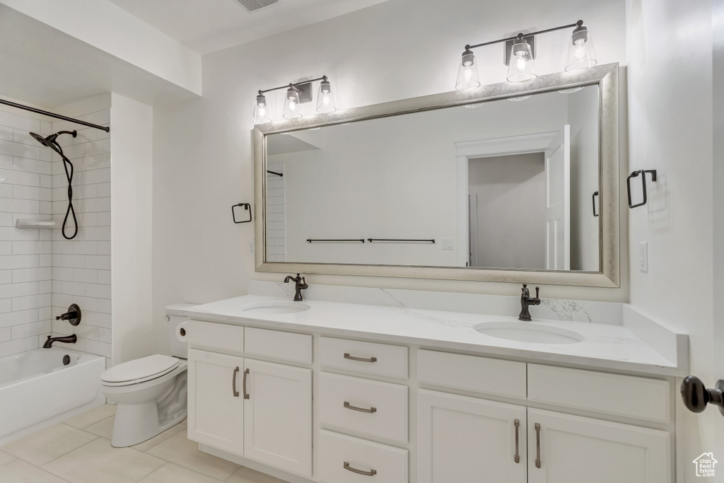 Full bathroom featuring dual vanity, tile floors, toilet, and tiled shower / bath combo