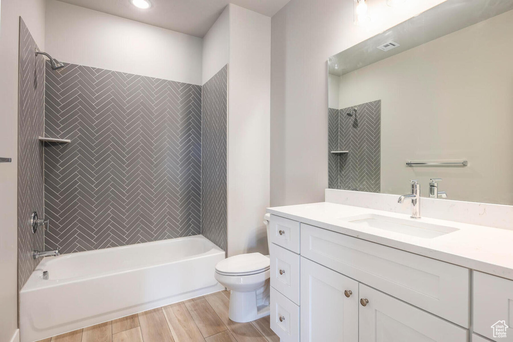 Full bathroom featuring hardwood / wood-style floors, toilet, tiled shower / bath, and vanity with extensive cabinet space