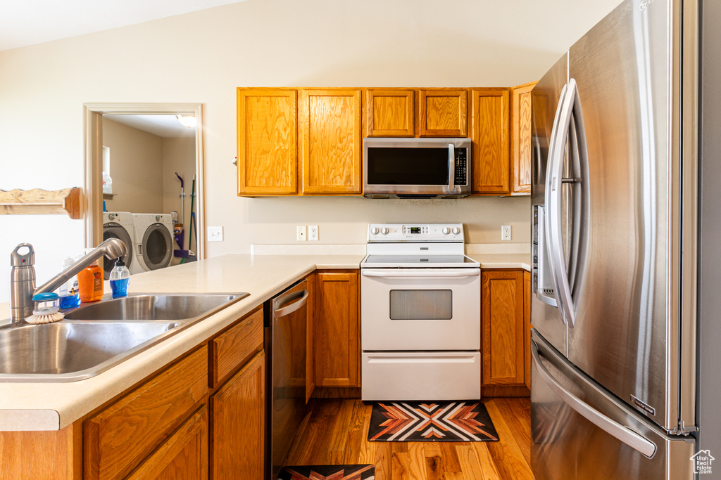 Kitchen with stainless steel appliances, sink, light hardwood / wood-style floors, lofted ceiling, and washer and dryer