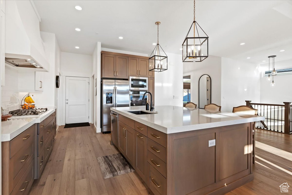 Kitchen with pendant lighting, a kitchen island with sink, wood-type flooring, premium range hood, and sink