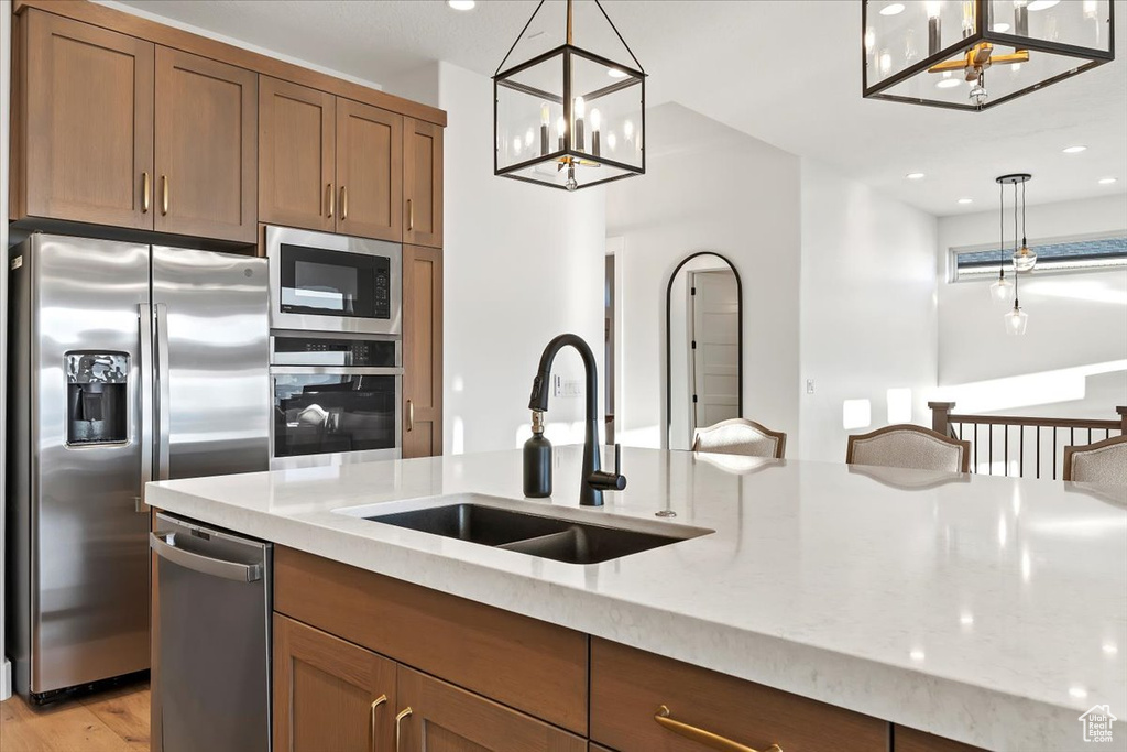 Kitchen featuring appliances with stainless steel finishes, sink, light hardwood / wood-style flooring, and decorative light fixtures