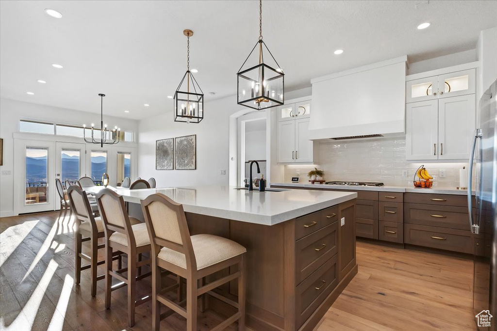 Kitchen featuring custom range hood, hanging light fixtures, light wood-type flooring, backsplash, and white cabinets