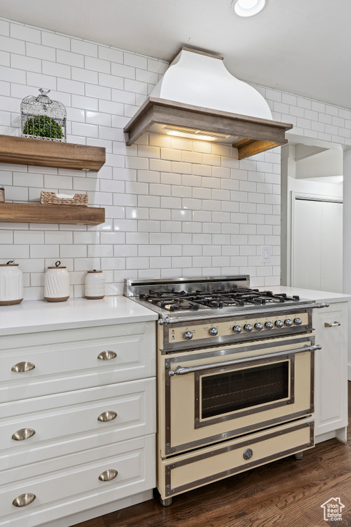 Kitchen with tasteful backsplash, dark wood-type flooring, range with two ovens, and white cabinets