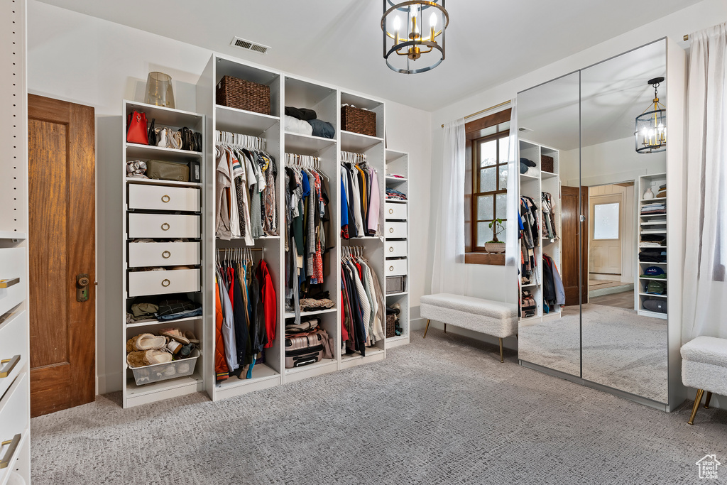 Walk in closet featuring an inviting chandelier and light carpet