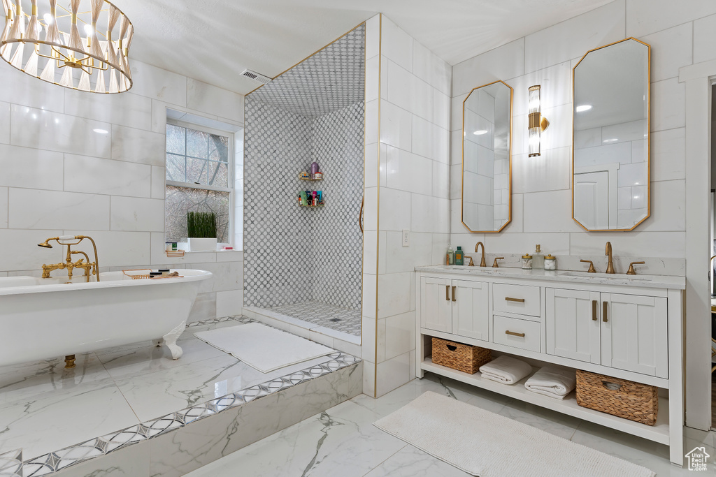 Bathroom with a notable chandelier, tile floors, tile walls, shower with separate bathtub, and double sink vanity