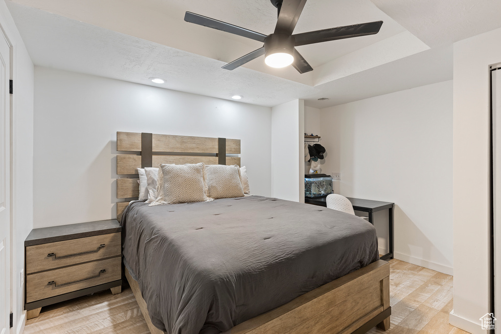Bedroom with ceiling fan, light hardwood / wood-style flooring, and a tray ceiling