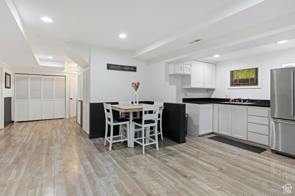 Kitchen featuring light wood-type flooring, stainless steel refrigerator, sink, and white cabinets